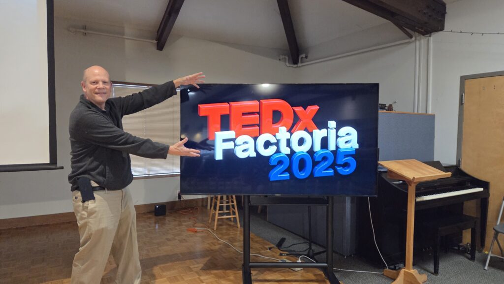 There I am, standing next to the big screen at TEDx Factoria 2025. Next time, I need to bring my sweater over my cell phone.